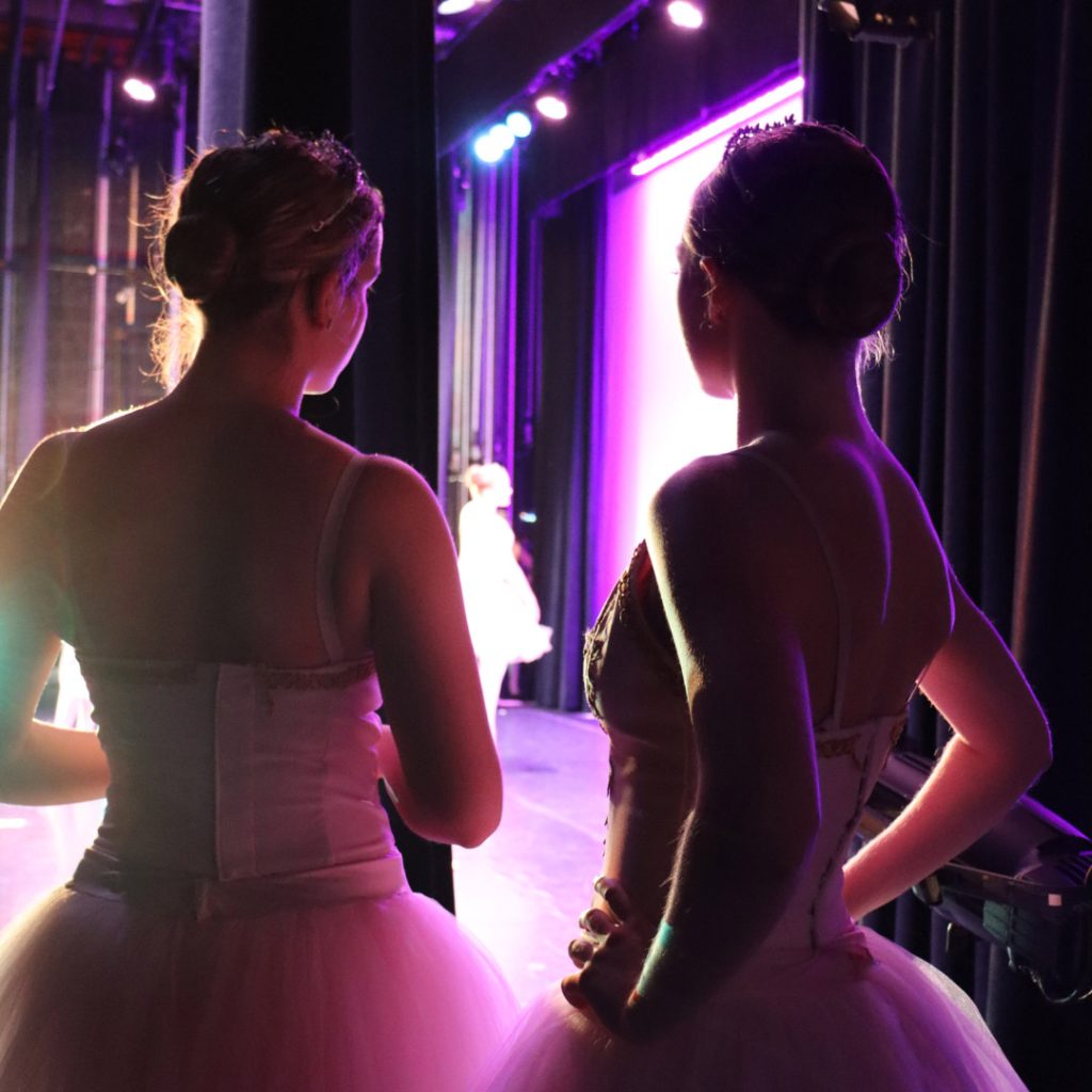 Two pre professional Steps dancers in tutus from behind waiting in the wings to go on stage
