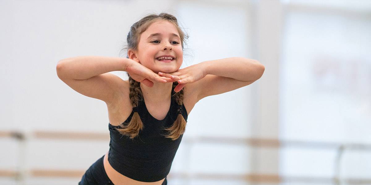 young female dancer in Steps studios - leaning forward with hands under her chin, elbows out and a big smile