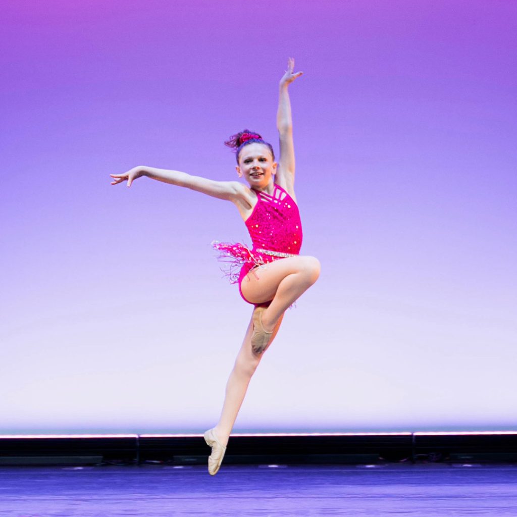 a single dancer in a hot pink dance outfit leaping across the stage in a steps youth division dance performance