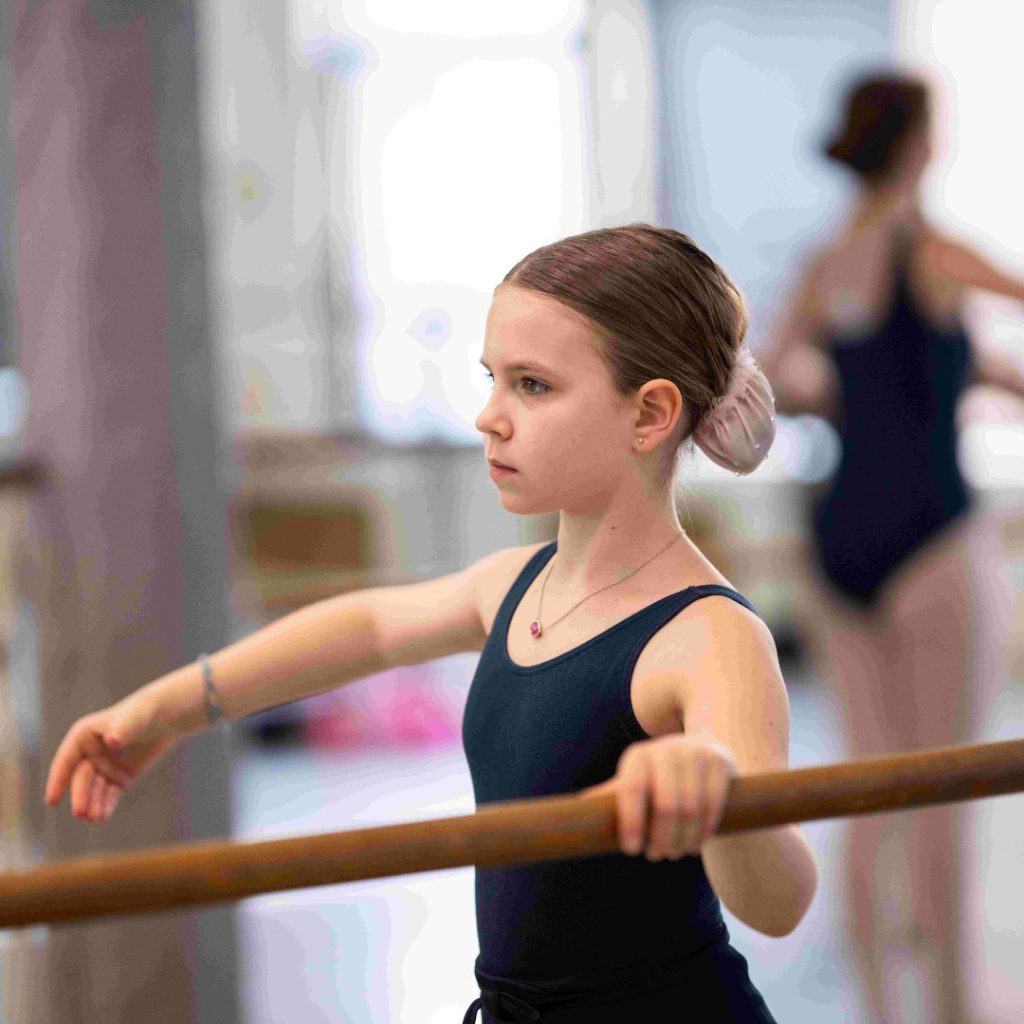 young ballerina looking serious and standing in profile at the barre