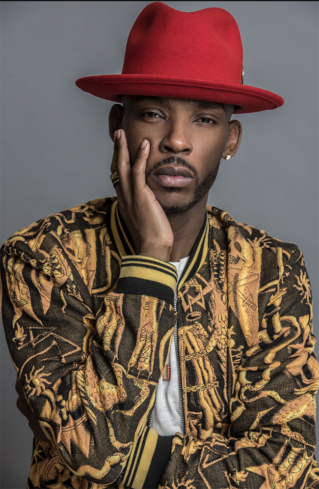 Jona Biddle headshot - fancy coat, red fedora