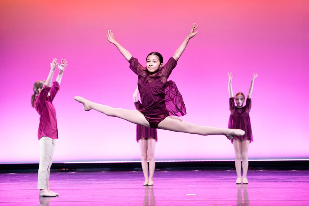 Steps Academy students in dance performance - three on stage in pink light and dark pink leotards and dance skirts