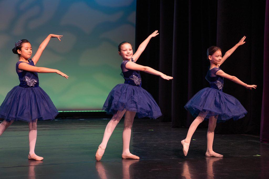 Steps Academy students in dance performance - three ballerinas on stage in dark blue leotards and tutus