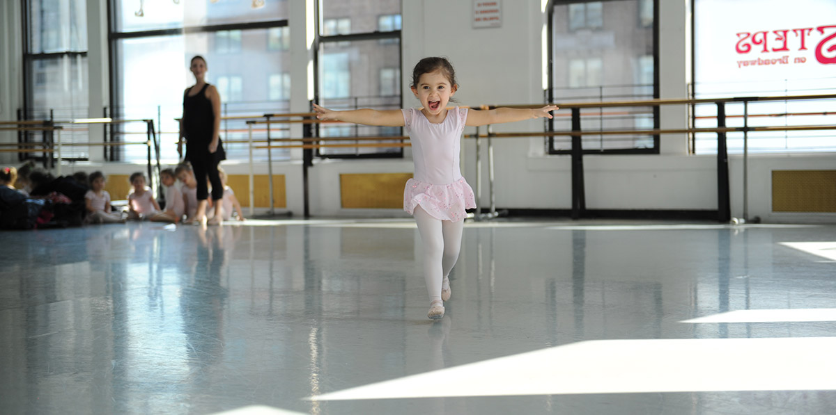 First Steps dancer, young girl running towards the camera across a dance studio in a pink leotard, tutu, and tights