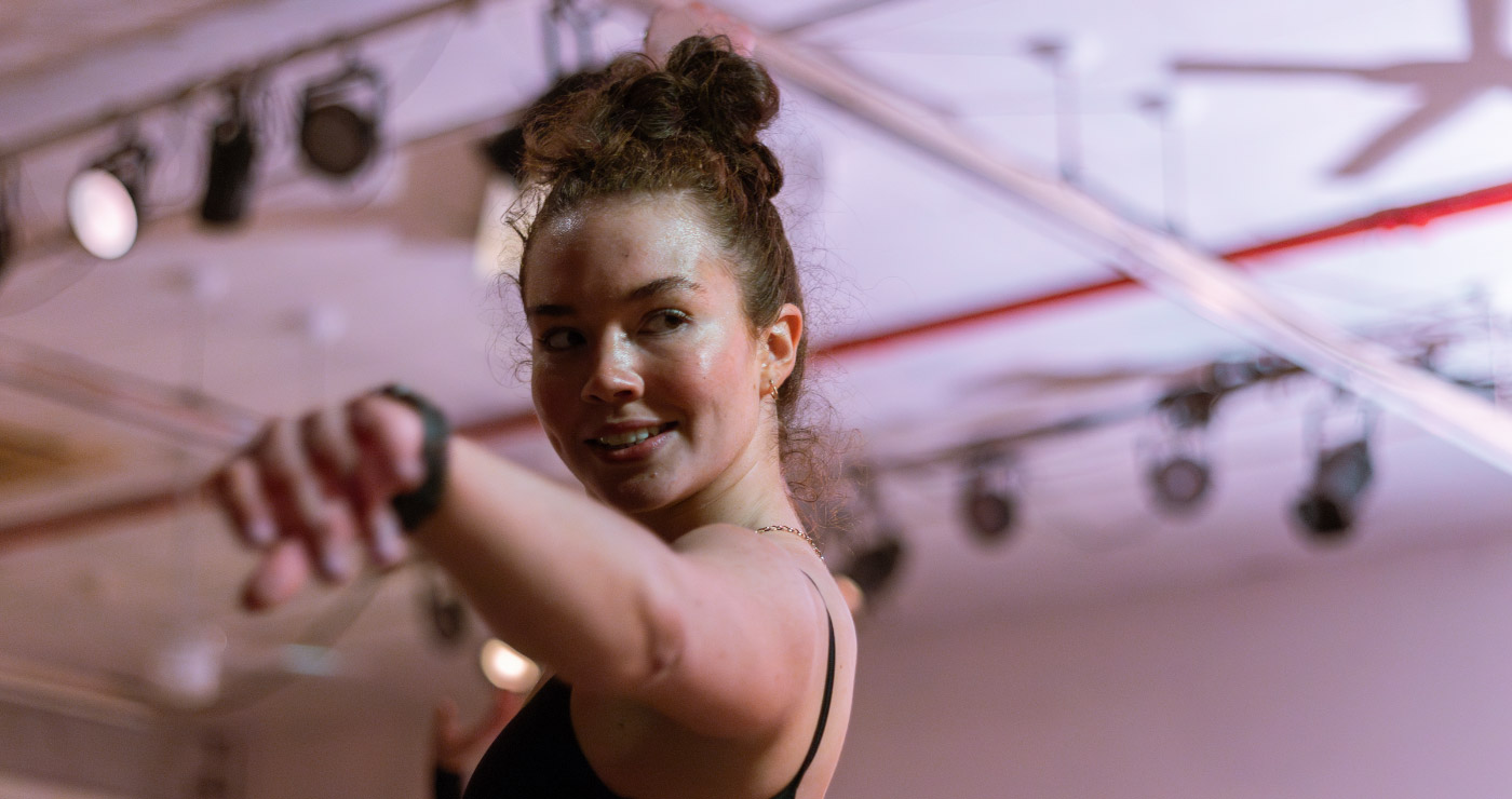 sweaty dancer from the chest up, smiling with her arm stretched toward the camera