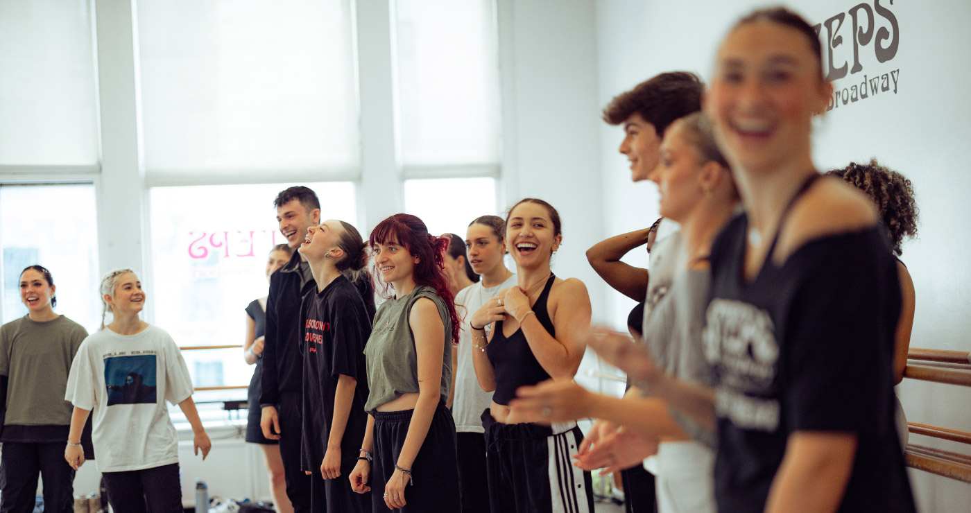 Dancers stand to the side of a studio at Steps - smiling and laughing