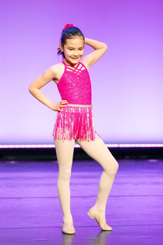 One Steps Academy dancer in a pink flapper-style costume on stage, knee bent and hand behind her head