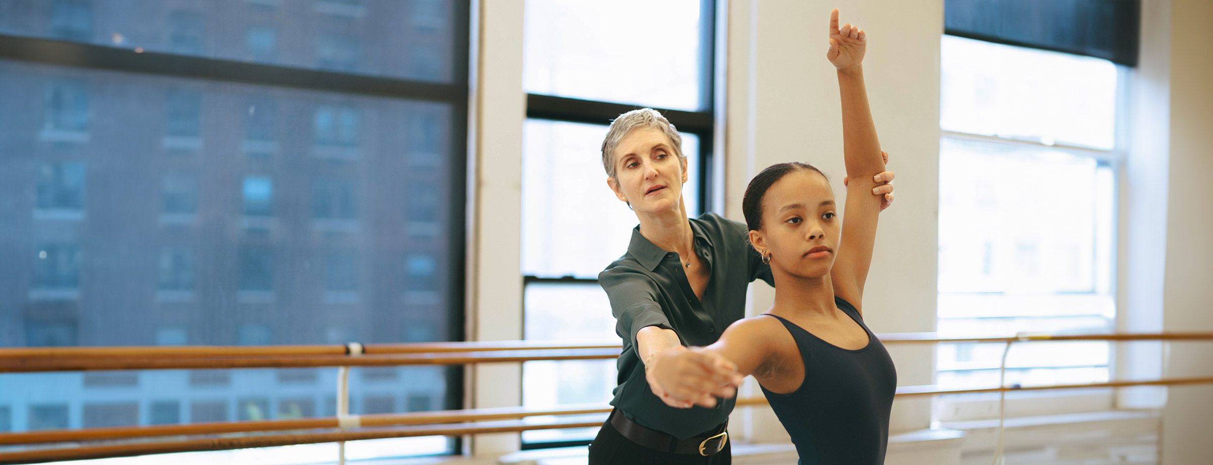 Jen  Kreichman, director of the Steps on Broadway Academy is assisting an academy dancer in Steps dance studios - New York City visible through the windows above the barre
