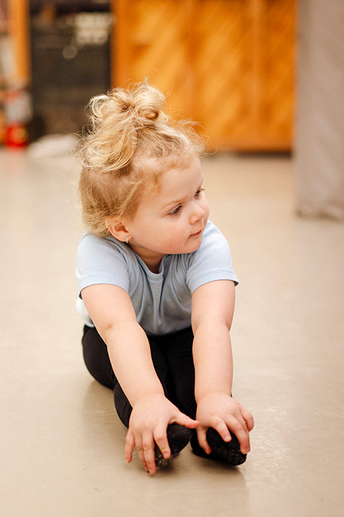 young dancer seated and reaching for her toes
