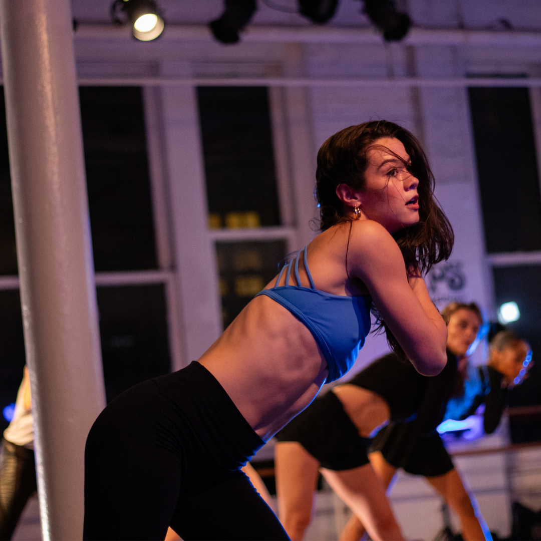 Dancer in blue bikini top and black jazz pants dancing in purple light in a Steps Spotlight dance class